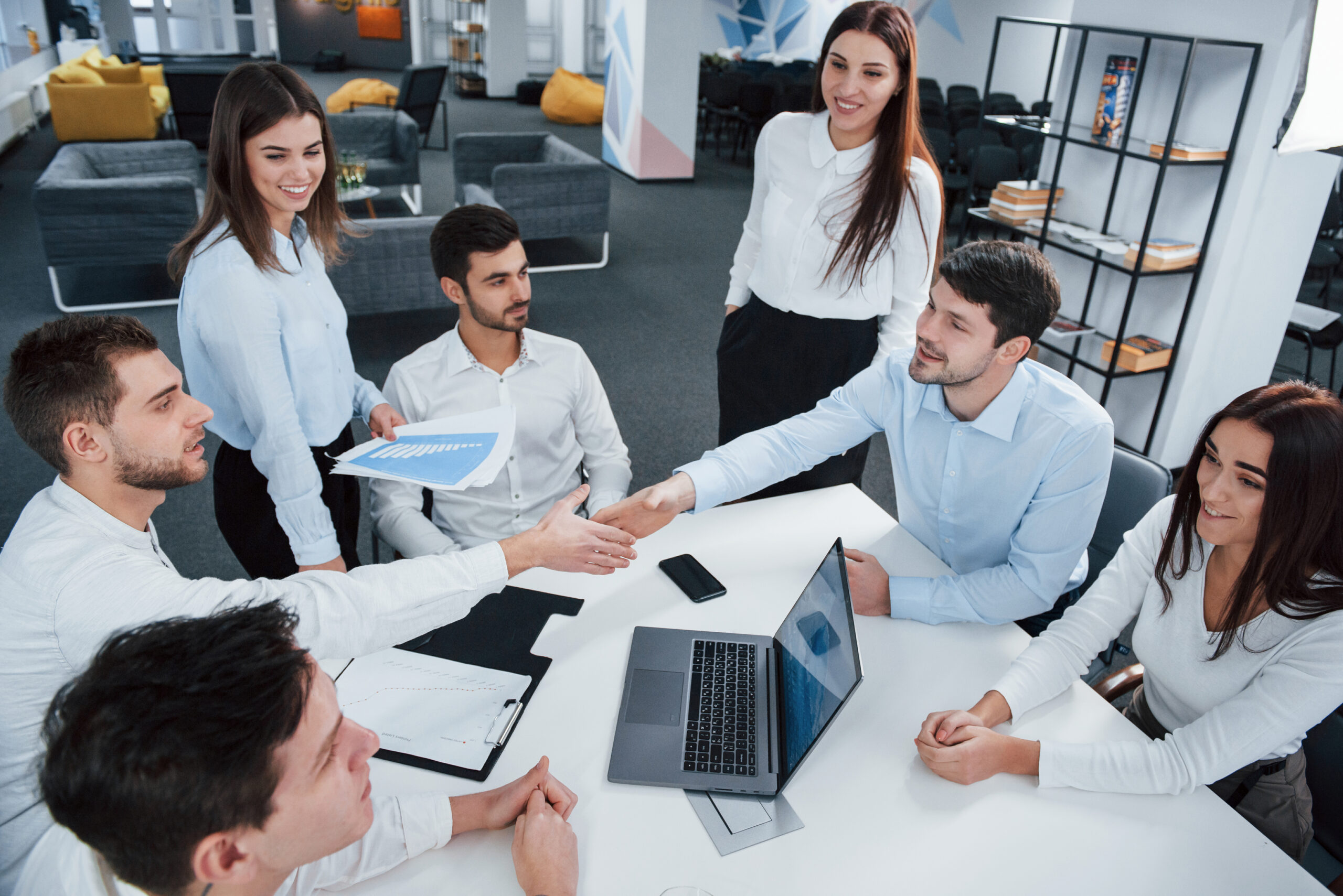 handshake-success-deal-top-view-office-workers-classic-wear-sitting-near-table-using-laptop-documents-scaled.jpg